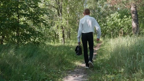 Junger Mann geht mit Rucksack auf einen Waldweg, umgeben von viel Grün