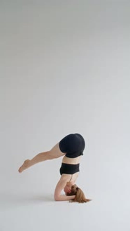 Young Woman Performing Headstand during Advanced Yoga Practice in White Studio