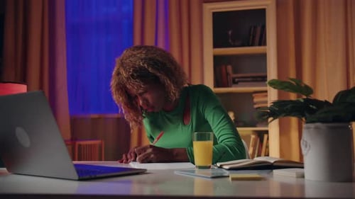 A Woman Studying at Night in a Cozy Home Office Surrounded By Books and a Laptop