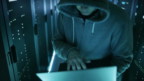 High Angle Shot of Computer Hacker in Hoodie, Holding Laptop. He Breaked in a Corporate Data Center