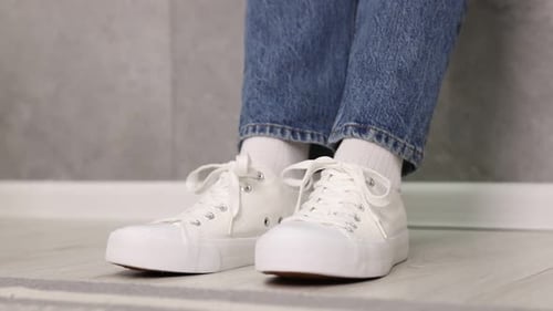 Woman adjusting shoelaces of white sneakers on indoors, closeup