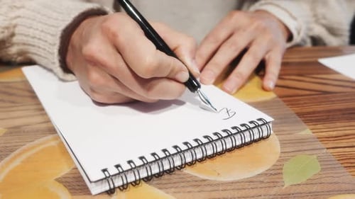 Hands writing in notebook with pen on wooden table.