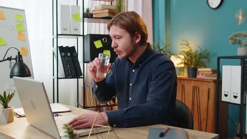 Businessman Sitting at Workplace Desk Drinking Water While Working with Laptop in Home Office