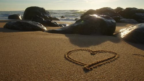 Beautiful heart drawn in the sand of a beach at sunset. Close up