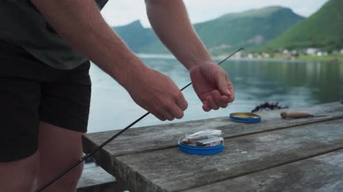 Man Threading Bait Onto Hook Of Fishing Rod By The Lake Shore. closeup