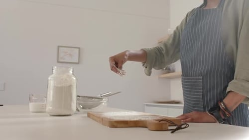 A young African American woman is sprinkling flour on a board with copy space