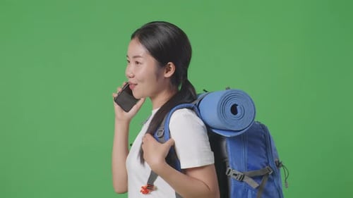 Side View Of Asian Female Hiker Backpack Talking On Smartphone While Walking On Green Screen