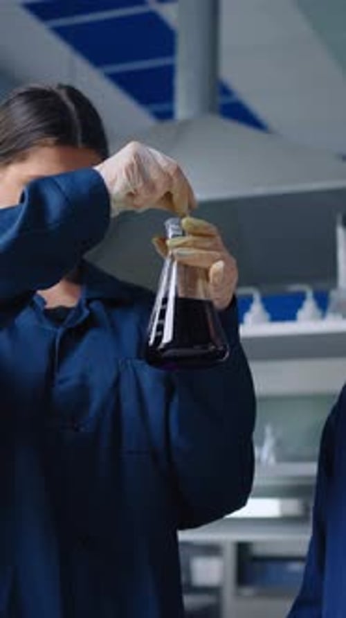 Junge Wissenschaftler untersuchen während der Durchführung sorgfältig dunkle chemische Lösung im Laborkolben