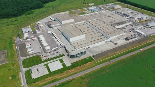 Contemporary factory with car parking. Industrial complex among green fields.