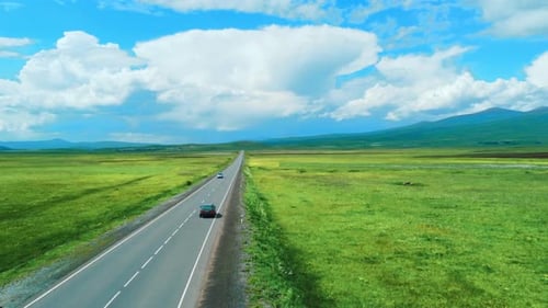 a car drives on asphalt road through green fields, mountains on sunny day,