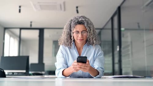 Happy Middle Aged Business Woman Holding Phone Using Cellphone in Office