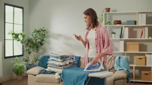 Woman Ironing Clothes While Using Mobile Phone