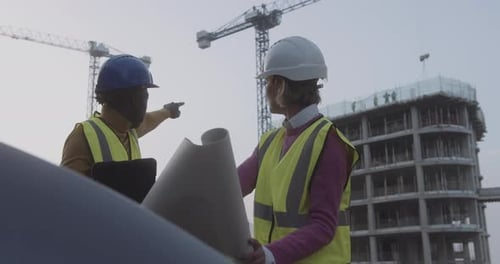 Civil Engineers meeting on building construction site discussing blueprint