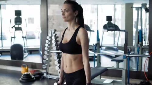 Brunette woman works out with dumbbells for strength and bodybuilding in gym close up