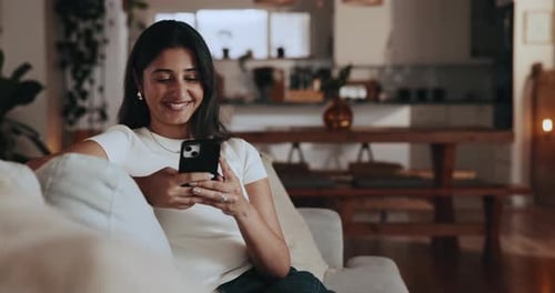 Smiling Woman Using Mobile Phone on Couch Indoors