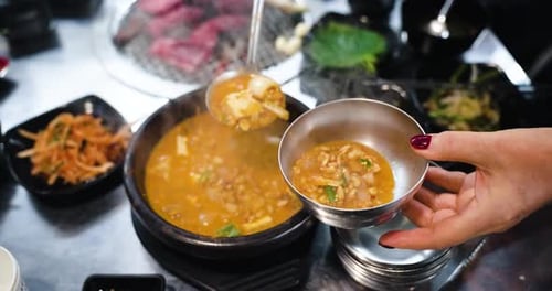 Servindo o ensopado de pasta de soja Doenjang Jjigae, cozido de uma panela quente em uma pequena tigela de metal