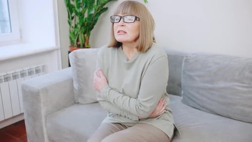 Mature Woman Sits With Abdominal Pain