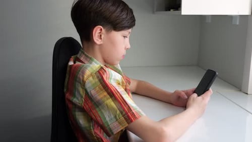 Boy Using Smartphone at Desk in Home