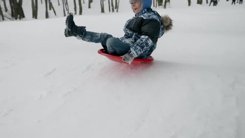 Slow motion footage of a young boy sledging down and jumping up on trampoline at a snow-covered hill