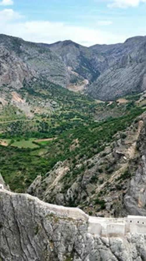 Aerial drone view of a historic fortress built along dramatic mountain cliffs overlooking a canyon v