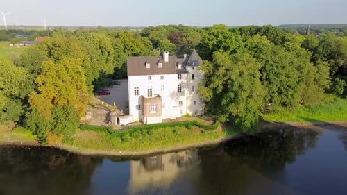 Histórico castillo blanco rodeado de un exuberante bosque verde, ubicado cerca de un río tranquilo. La vista aérea