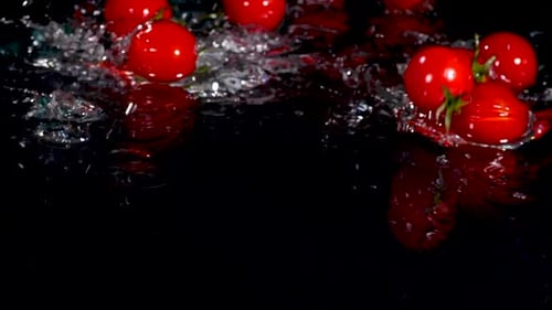 Tomaten fallen mit einem Spritzer ins Wasser und Blasen auf schwarzem Hintergrund
