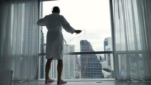 Man in bathrobe listening to music at window