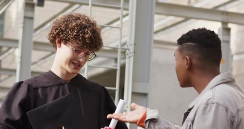No campus, diversos amigos estendendo a mão acionam o graduado, recuperando o diploma e comemorando.