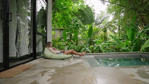 Multiracial Woman Relaxes By Poolside Lounges with Laptop in Tropical Garden Casual Remote Work