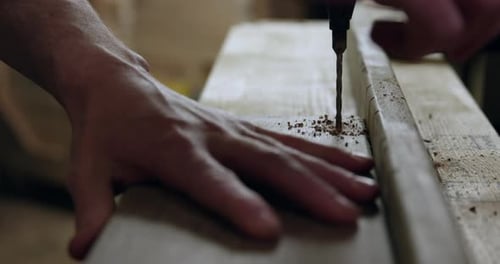 Man using drill press to make hole in piece of wood - close up on hands