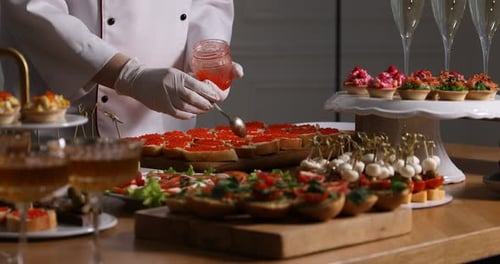 Chef making sandwiches with red caviar for buffet at table indoors, closeup
