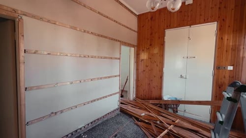 Room under renovation with stripped wall panels and construction debris, home remodeling interior