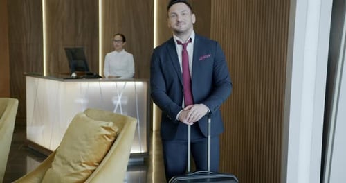 Portrait of Businessman Standing in Hotel Lobby Holding Suitcase Smiling