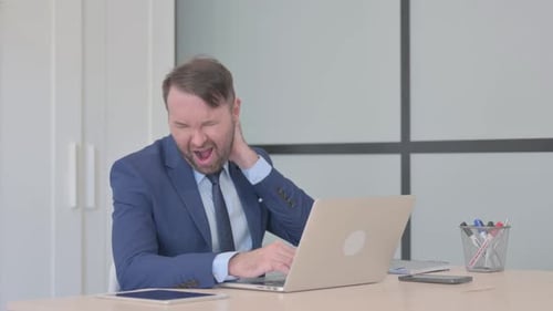 Man Rubbing Neck While Working At Laptop