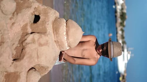 VERTICAL VIDEO POV Happy Tanned Male Teenager in Straw Hat Building Sand Castle Sunny Seaside Resort