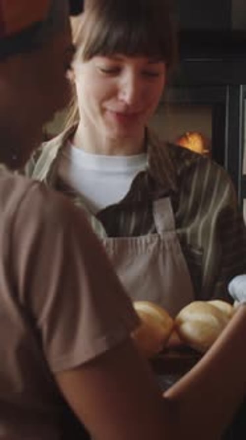 Happy Women Exchanging Fresh Baked Rolls in Bakery