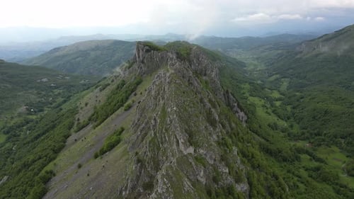 Flying over beautiful green mountains. In the background, stone cliffs with snow are visible.