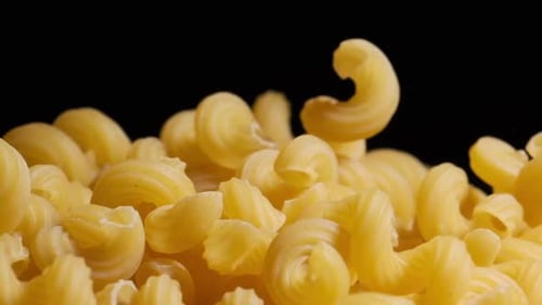 Raw macaroni pasta falls gracefully in stunning slow motion.