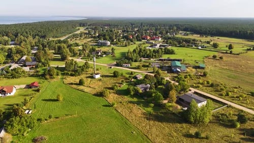 Small Latvian neighborhood in Jurkalne during sunny day. Houses and homes with farm field and main s
