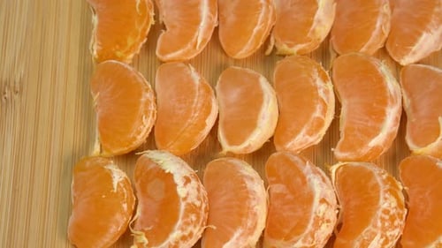 Tangerine on wooden board lie in row and rotate. Mandarin fruit slices close up