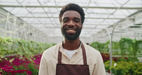 Smiling Young Adult in Greenhouse Surrounded by Flowers