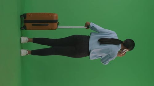 Asian Woman With Luggage Talking On Smartphone While Walking And Standing In The Green Screen