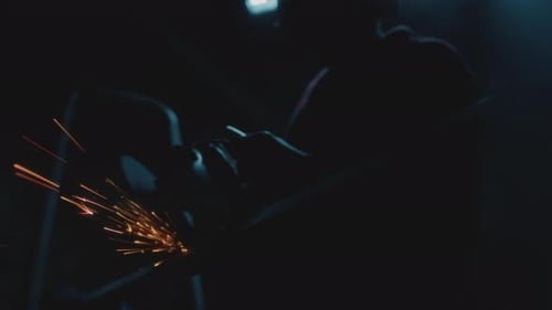 Worker Grinding Metal With Sparks in Dark Workplace