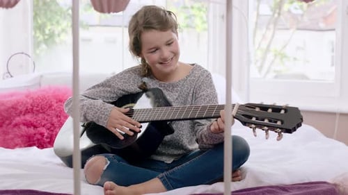 Girl Playing Guitar on Bed in Sunny Room
