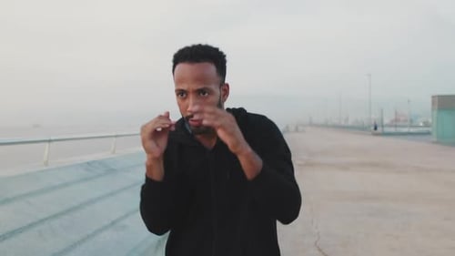 Young athlete boxer practicing punching technique while standing on the embankment