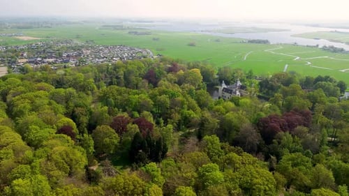 Aerial view of a historic castle surrounded by a forest, with vast green fields, winding waterways