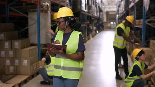 Professional female supervisor in safety gear managing logistics operations, coordinating workers an