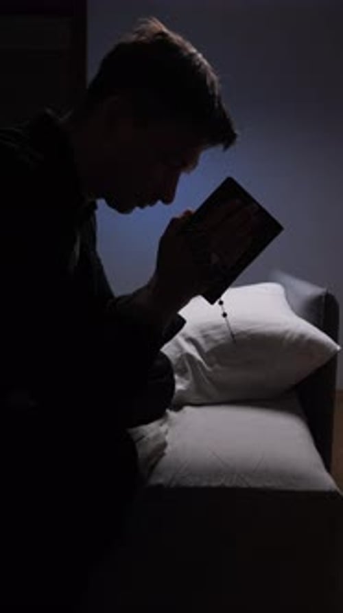 Man Praying with Rosary Beads in Dark Bedroom