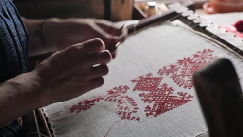 A close-up of a needle passing through the canvas and pulling a red thread behind it.