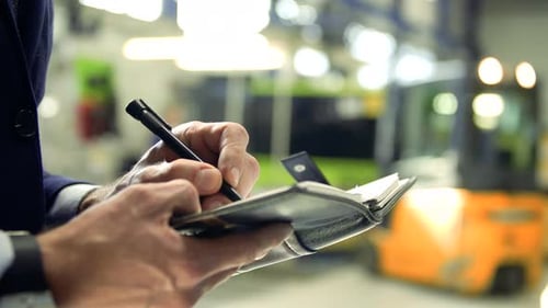 An Industrial Man Engineer Standing in a Factory, Writing Notes in A